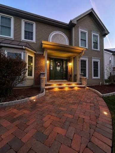 Curved brick paver walkway with step lighting leading to a front door